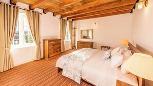 A bedroom with a wooden ceiling, a bed with a floral bedspread, a nightstand, a dresser, and a window with curtains.
