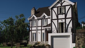 A two-story house with a stone chimney, white exterior with dark trim, and a garage door.