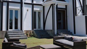 A large house with a white exterior and dark trim, featuring a front porch with wicker furniture and a small covered area.