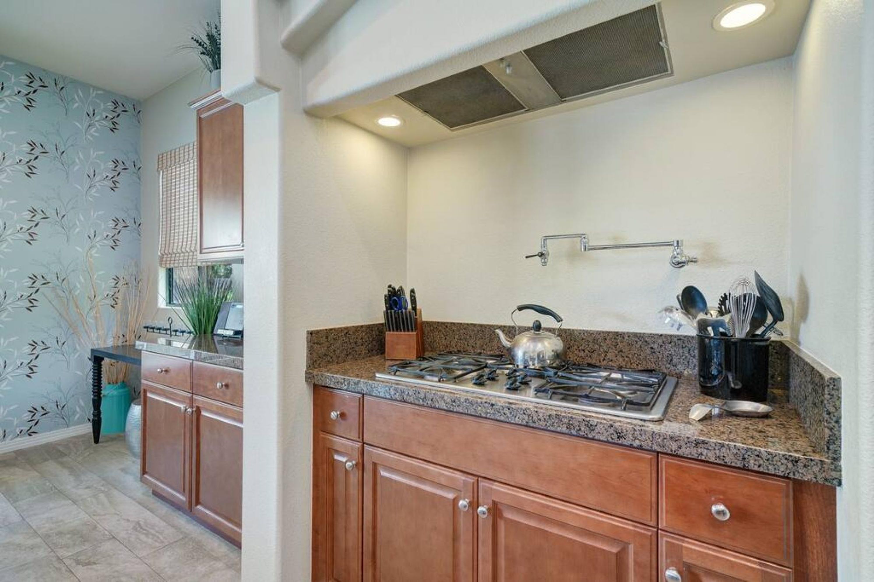 A kitchen with a gas stove, wooden cabinets, and a window with blinds.