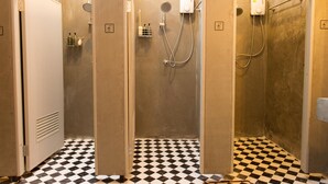 Casa de banho com três cabines de duche, cada uma com um chuveiro e um pulverizador de mão. O chão tem um padrão xadrez preto e branco.