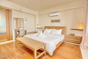 A hotel room with a wooden floor, a bed with white linens, a wooden nightstand, a bedside table, a mirror, and an air conditioning unit on the wall. - Mayumi Beach Villa (Boracay Island)