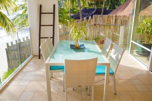 A glass-top dining table with wicker chairs and blue cushions, surrounded by a bamboo fence and potted plants.