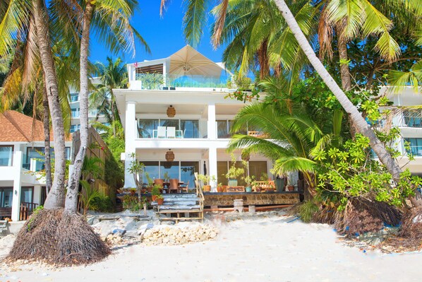A beachfront hotel with a two-story structure, outdoor seating area, and palm trees.