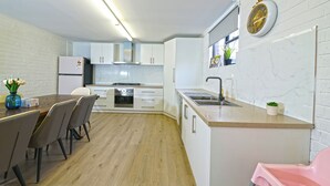 A modern kitchen with white cabinets, a wooden dining table, and a pink chair.