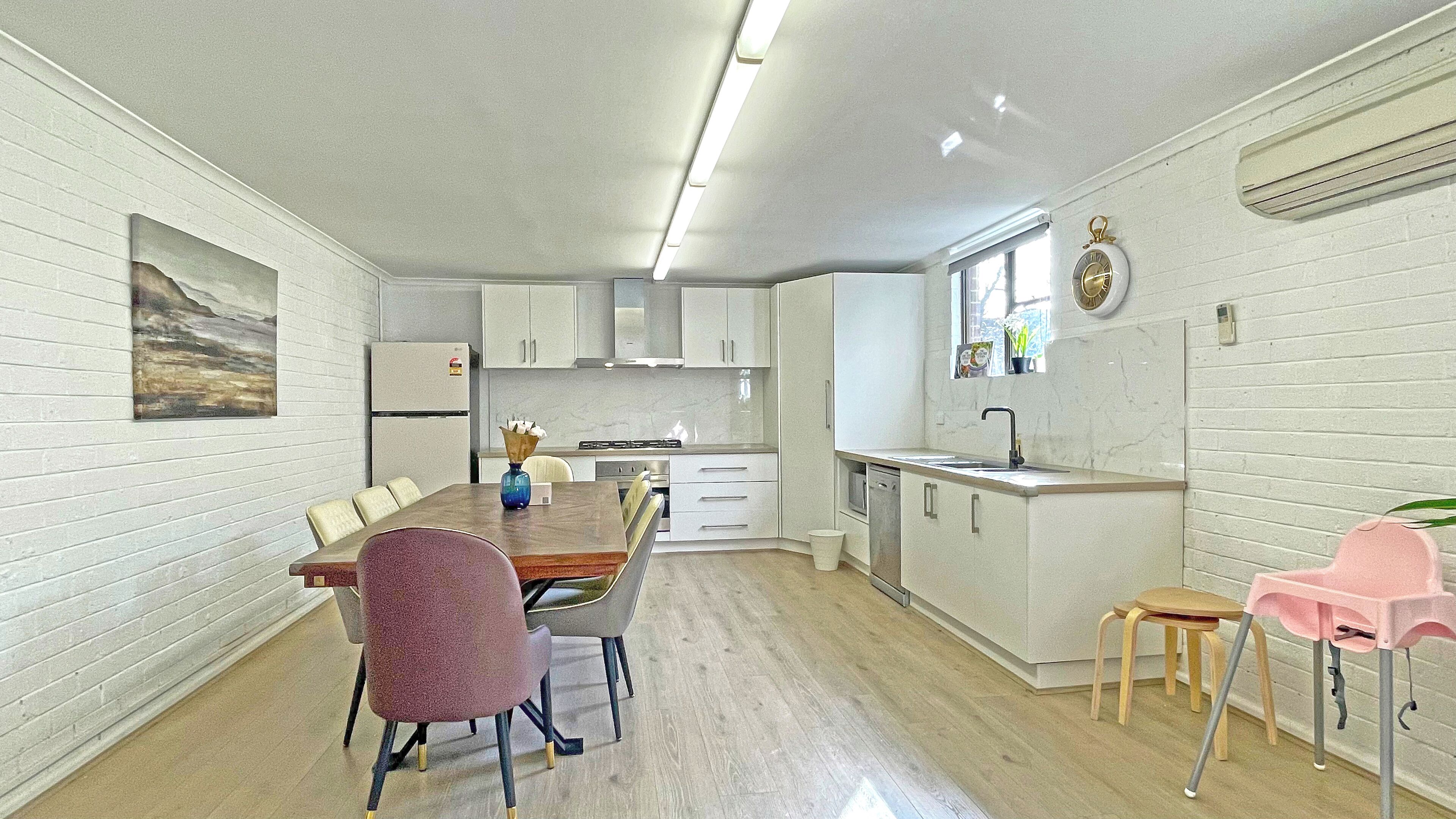 A modern kitchen with white cabinetry, a dining area with a wooden table and chairs, and a small island with a sink.