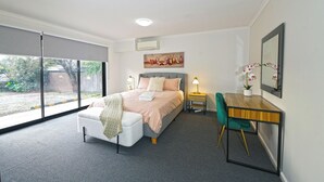 A bedroom with a bed, a desk, a chair, a window, and a small table with a plant.