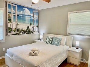 A neatly arranged bedroom with a bed, two bedside tables, and a window with a beach mural. - Spacious 3BR High Point Stay | HPU & Foosball (High Point)
