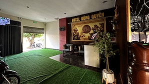 Ein Hotel-Empfangsbereich mit einer Rezeption, einer großen Wanddekoration und einem Boden aus Kunstgrün.