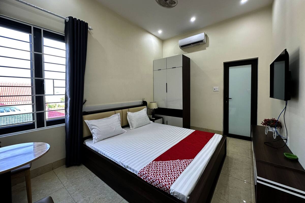 Habitación de hotel con cama, escritorio, silla, equipo de aire acondicionado, televisor y ventana con cortinas.
