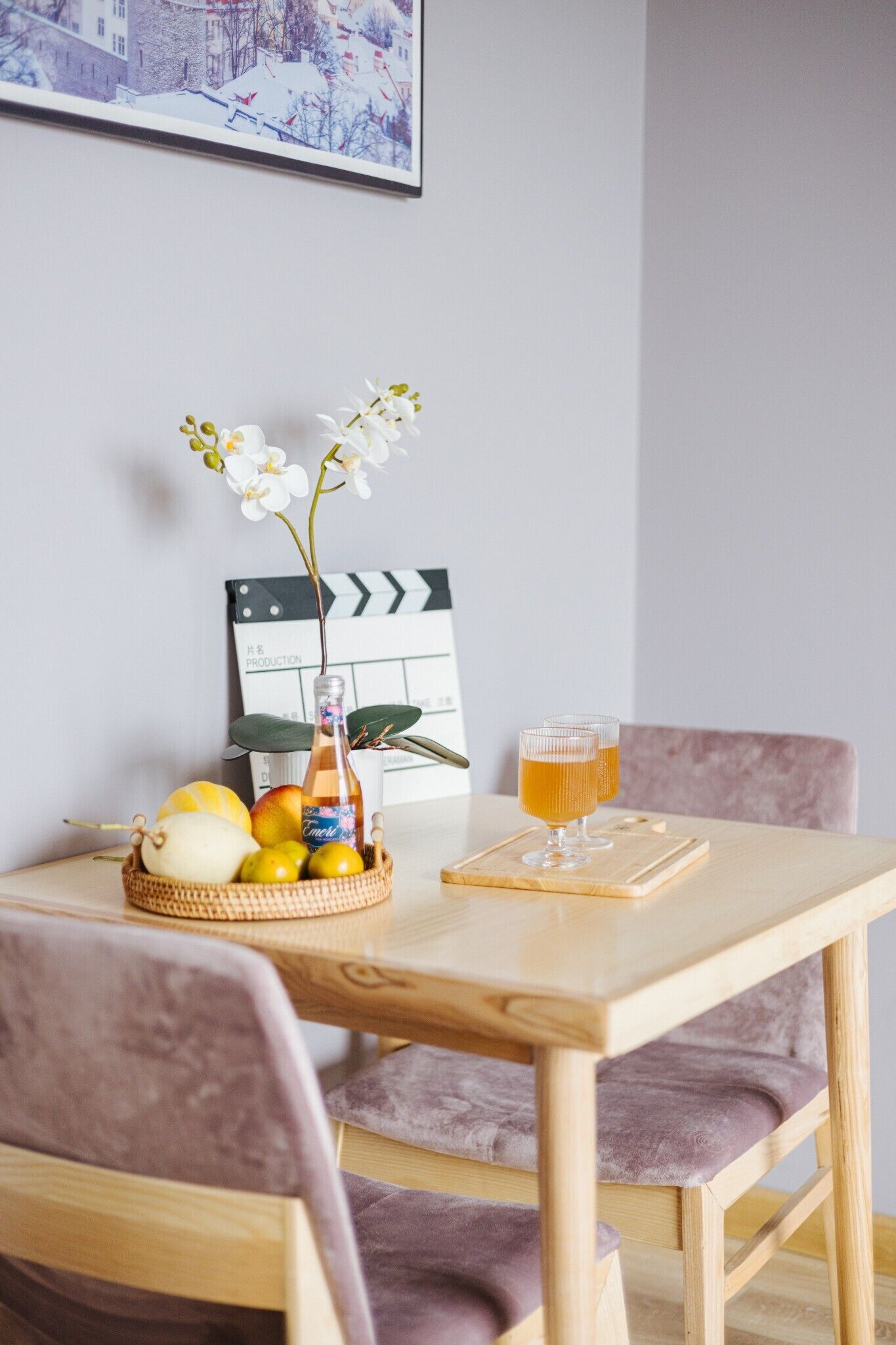 Ein Holztisch mit einem Klapperbrett, einer Weinflasche, einer Obstschale und zwei Orangensaftgläsern.