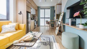 A compact living space with a yellow sofa, a dining area, a kitchen, and a TV mounted on the wall. - Crescendo Urban Stay (Hanoi)