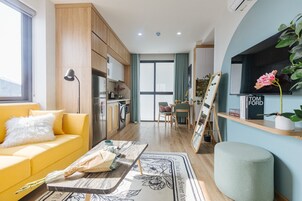 Un espacio habitable compacto con sofá amarillo, zona de comedor, cocina y televisor montado en la pared.