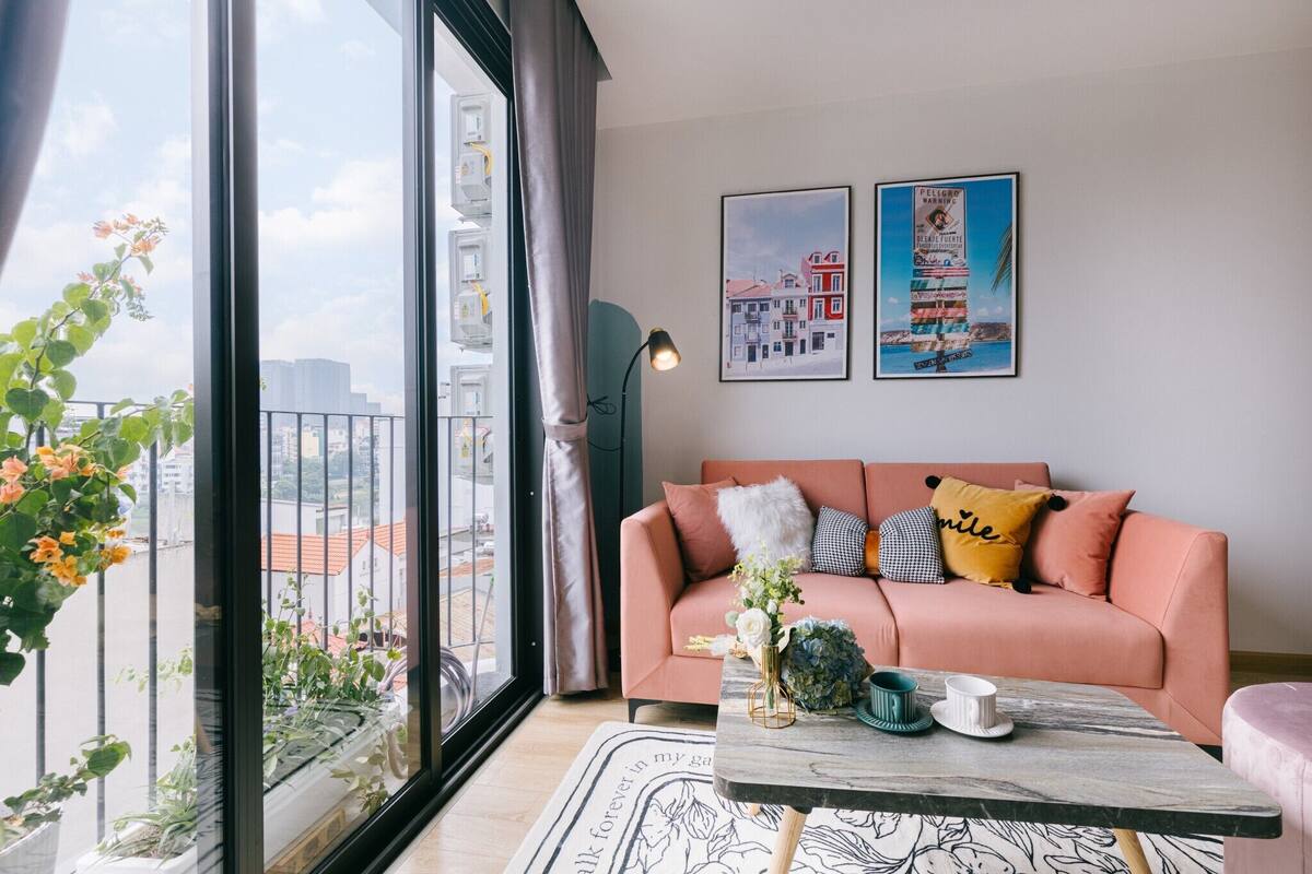 A modern living room with a pink sofa, a coffee table, and a large window offering a city view.