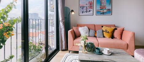 A modern living room with a pink sofa, a coffee table, and a large window offering a city view.