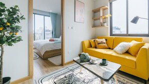 A modern living room with a yellow sofa, a coffee table, and a view of the city through large windows. - Crescendo Urban Stay (Hanoi)