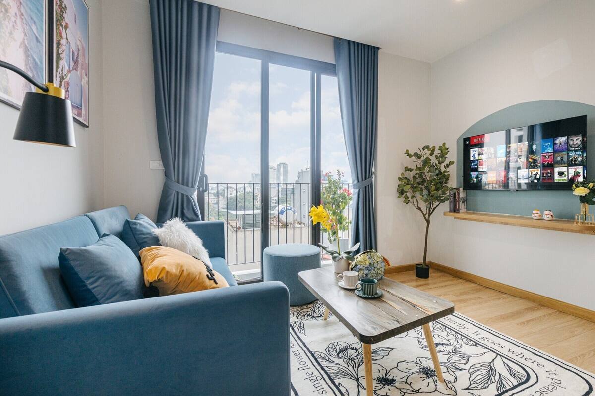 A modern living room with a sofa, a coffee table, and a large window with curtains.