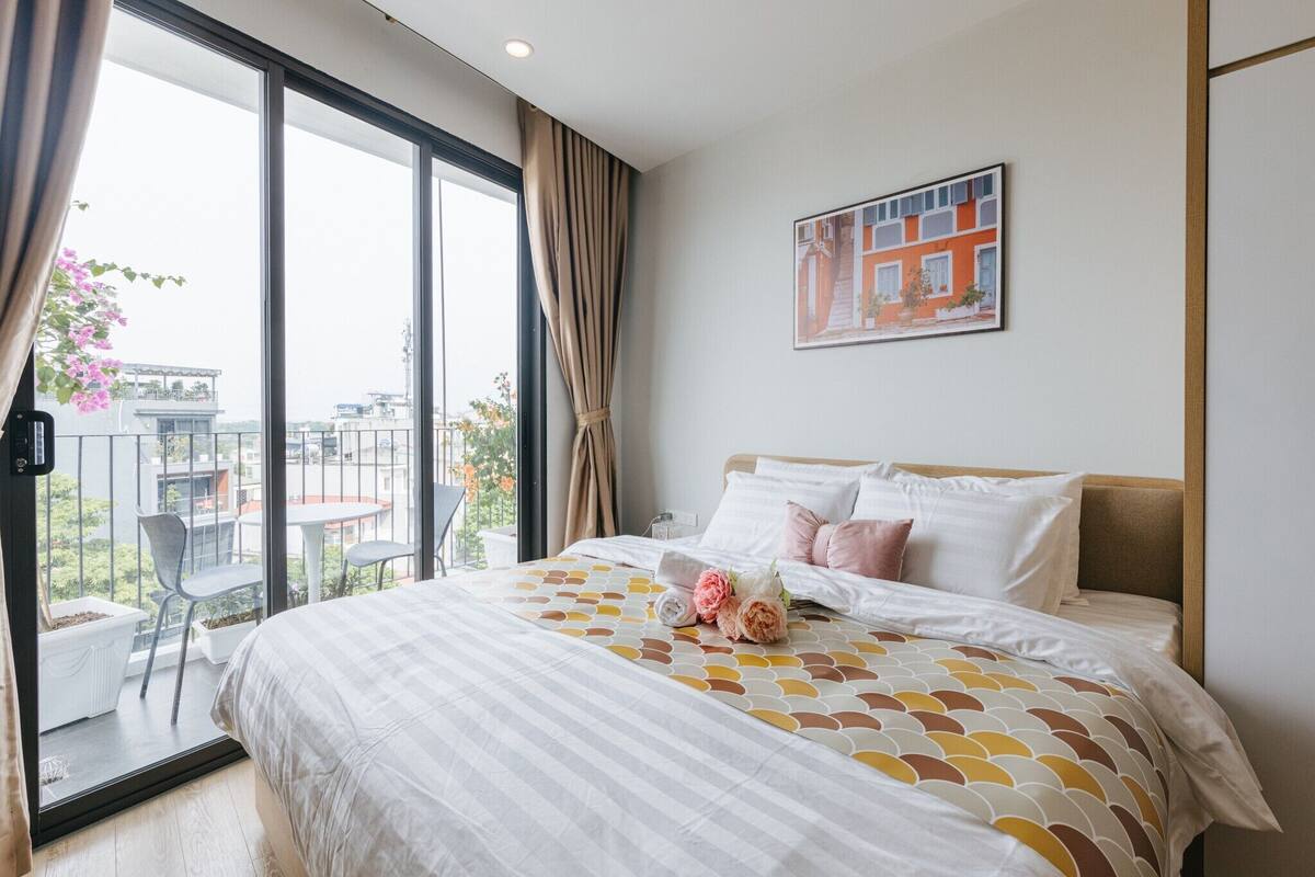 A hotel room with a large bed, a balcony with chairs, and a painting on the wall.