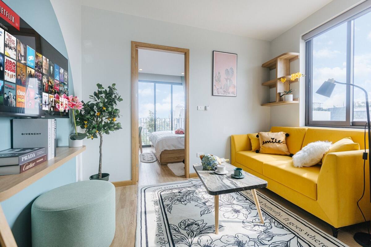 A modern living room with a yellow sofa, a coffee table, a bookshelf, and a large window.