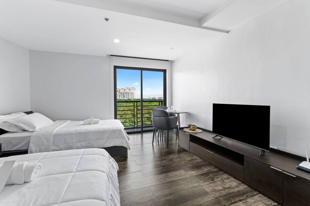 A modern hotel room with two beds, a TV, a desk, and a balcony with a city view.