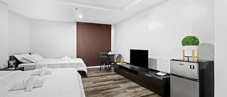Quarto de hotel moderno com duas camas, TV de tela plana, geladeira e um pequeno espaço para sentar.