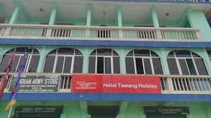 Een meerhoog gebouw met balkons, een bord met 'Hotel Tawang Holiday' en een 'TAXMI GROCERY' winkel.