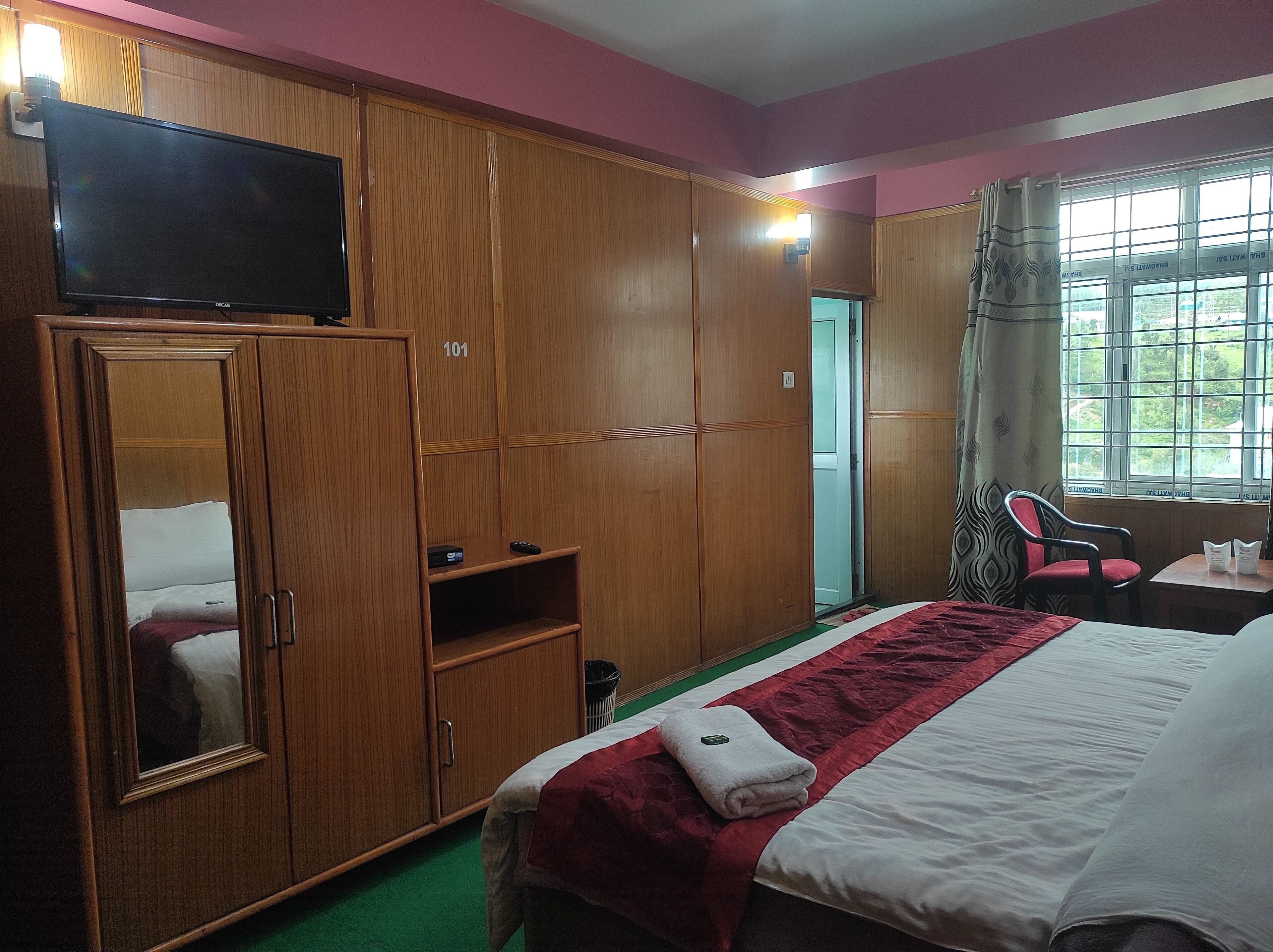 A hotel room with a bed, a wardrobe, a television, a window with curtains, and a small table.