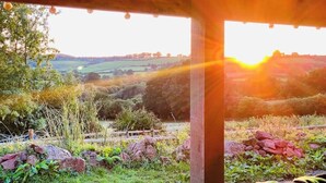 Une pergola en bois offrant une vue sur un paysage rural au coucher du soleil.