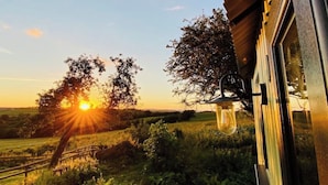 Une vue sur le coucher de soleil, prise depuis une fenêtre, avec une lanterne suspendue, une clôture en bois et des arbres au premier plan.