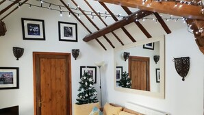 A cozy living room with a wooden door, a Christmas tree, a sofa with cushions, and a flat-screen TV on a stand. - The Stables w/Hot tub, amazing views, English Bicknor Forest of Dean (Coleford)