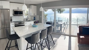 A modern kitchen with a large island, stainless steel appliances, and a view of the sea through large sliding doors.