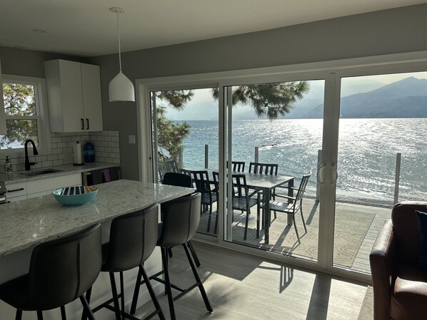 A modern kitchen with a large island, bar stools, and a dining area with a view of the sea. - Seclusion Bay Resort 9. Luxury Lakeside Paradise, beachfront on Okanagan Lake. (West Kelowna)