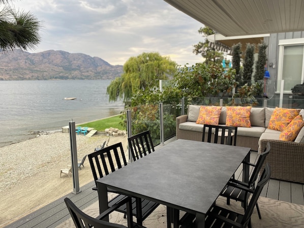 Um terraço com mesa e cadeiras, com vista para um lago e montanhas ao fundo.