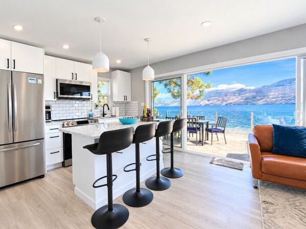 A modern kitchen with a central island, bar stools, and a view of the sea.