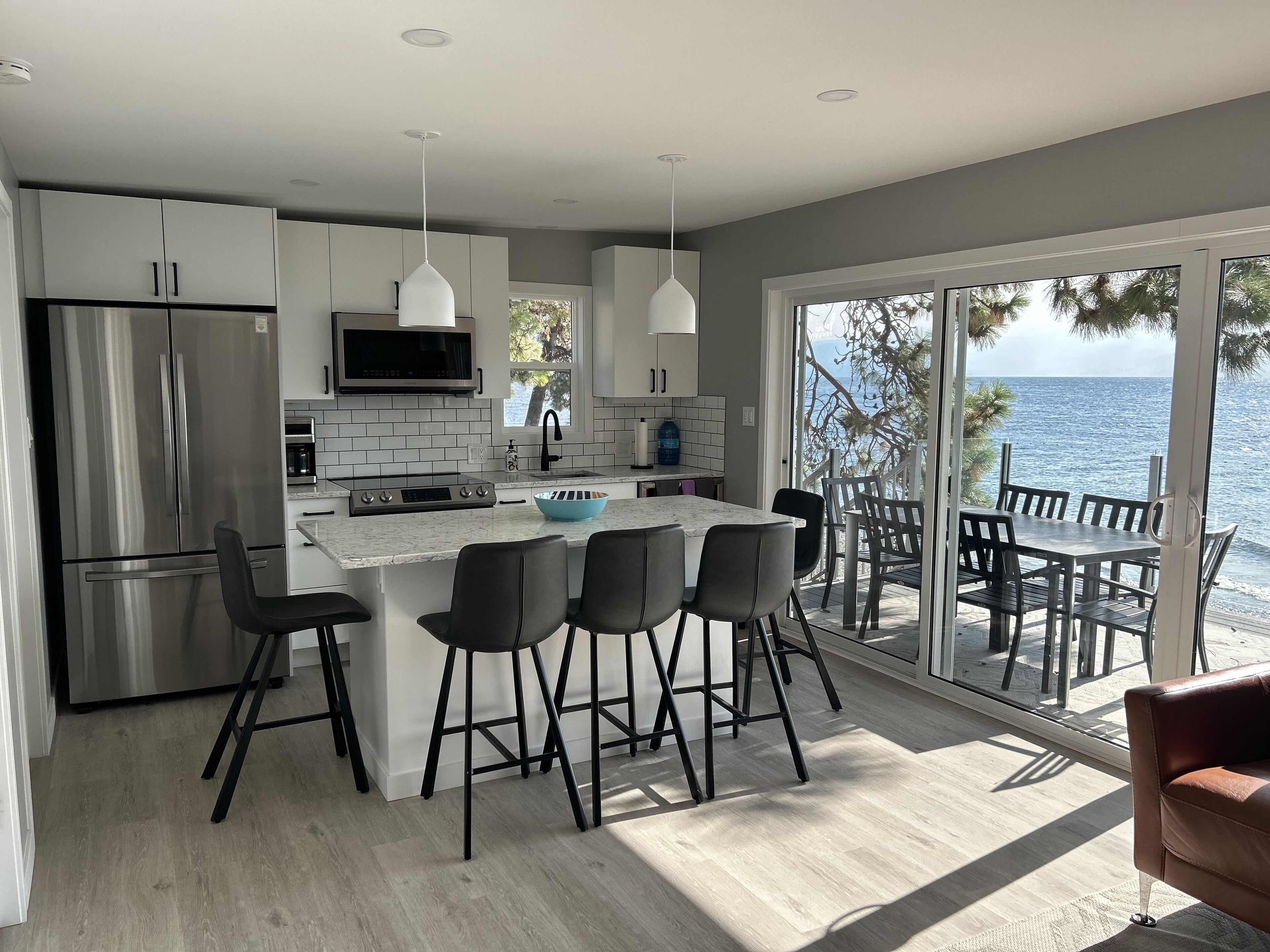 Une cuisine moderne dotée d’un grand îlot central, d’appareils électroménagers en acier inoxydable et offrant une vue sur la mer grâce à de grandes portes coulissantes.