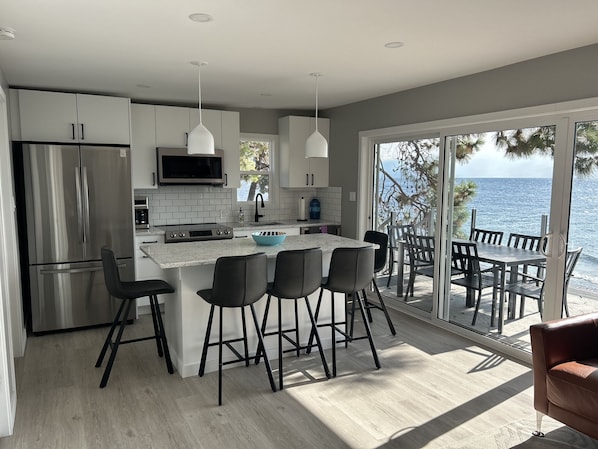 Una cocina moderna con una isla grande, electrodomésticos de acero inoxidable y vistas al mar a través de amplios ventanales correderas.
