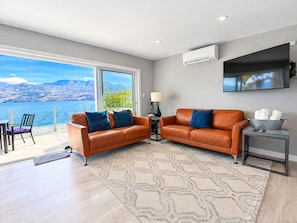 A modern living room with two leather sofas, a flat-screen TV, and a view of a lake. - Seclusion Bay Resort 9. Luxury Lakeside Paradise, beachfront on Okanagan Lake. (West Kelowna)
