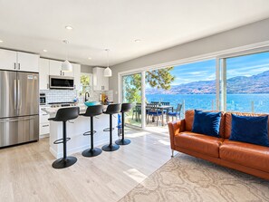 A modern kitchen with stainless steel appliances, a dining area with bar stools, and a large window overlooking a lake.
