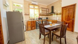 A modern kitchen with a dining table and chairs, a refrigerator, a washing machine, and wooden cabinets. - MacMillan's Holiday Villas await you offering a modern living space (Grand Anse Praslin)