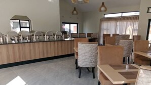 A modern dining area with a long counter, cushioned chairs, and pendant lighting. - Olive Comfort Boutique Luxury Suites (Kwekwe)