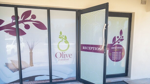 A reception area with a glass partition displaying the logo and name 'Olive Comfort' and 'luxury suites'. - Olive Comfort Boutique Luxury Suites (Kwekwe)