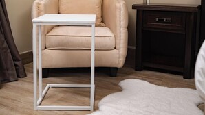 A beige sofa with a white table in front, a dark wooden nightstand, a white furry rug, and a wall-mounted light fixture. - Olive Comfort Boutique Luxury Suites (Kwekwe)