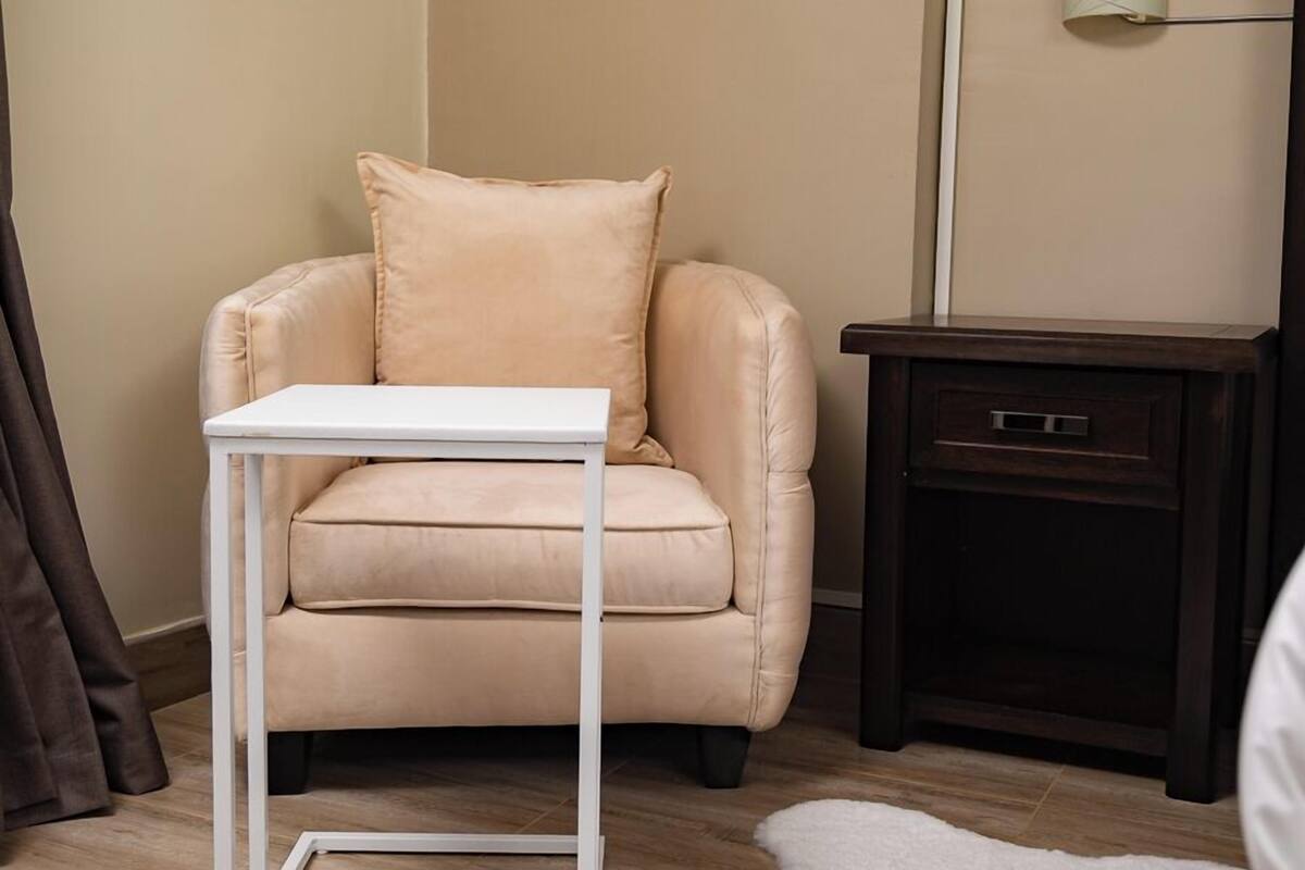A beige sofa with a white table in front, a dark wooden nightstand, a white furry rug, and a wall-mounted light fixture.