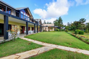 A modern building with a covered patio area, a well-maintained lawn, and a stone pathway. - The Walden (Nuwara Eliya)