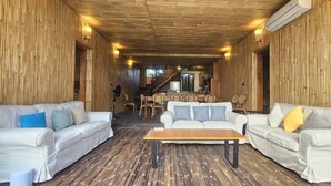 Une pièce aux murs lambrissés, avec deux canapés blancs, une table basse en bois et un escalier menant à un espace repas.