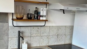 Moderni keittiö, jossa on kaksi allasta, musta hana ja yläpuolella hylly, jossa on lasi, pullo ja säilytysastia.