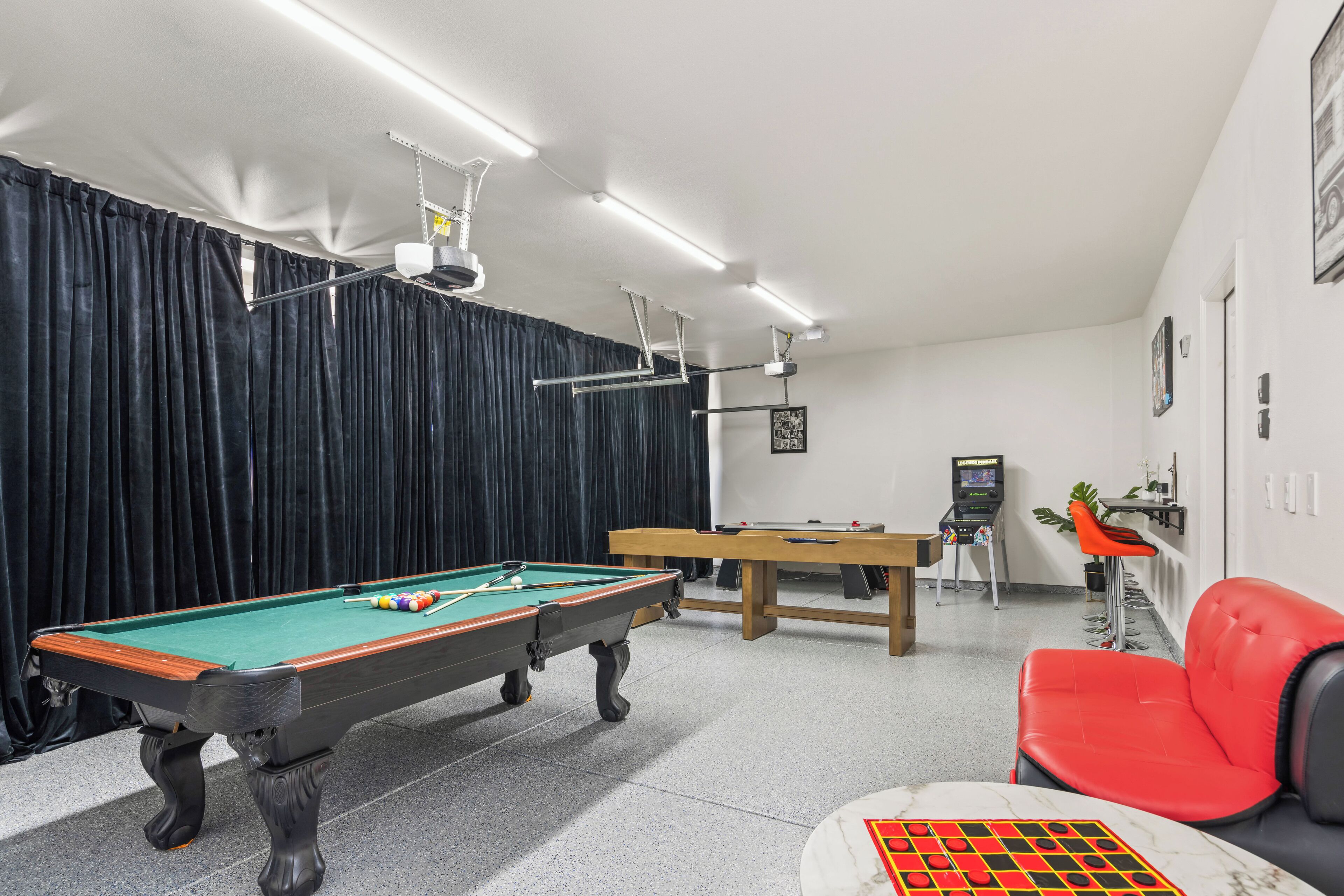 A pool table, a billiards table, a red chair, and a small table with a checkered pattern.