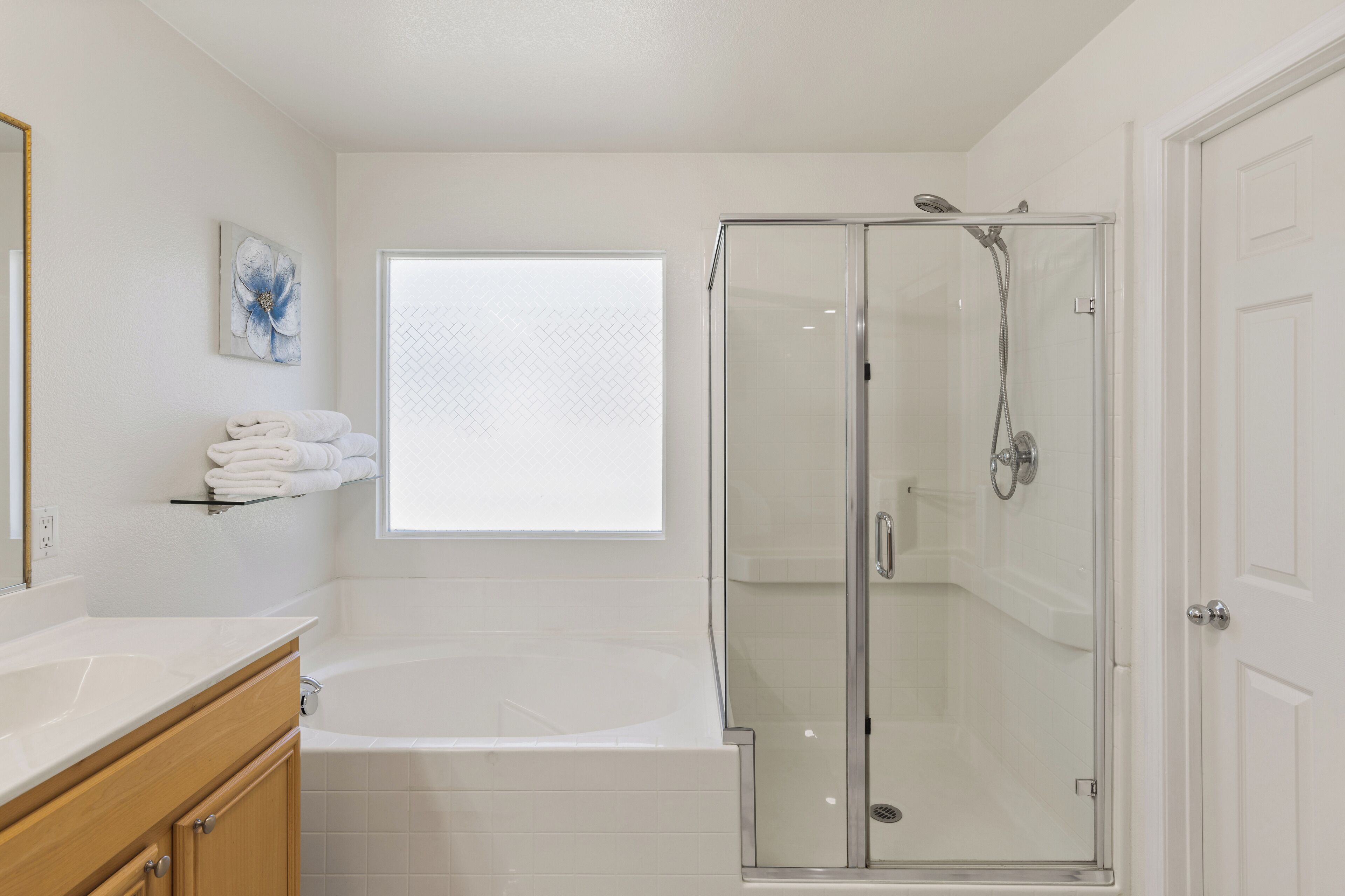 A modern bathroom with a glass-enclosed shower, a large window, and a white vanity.