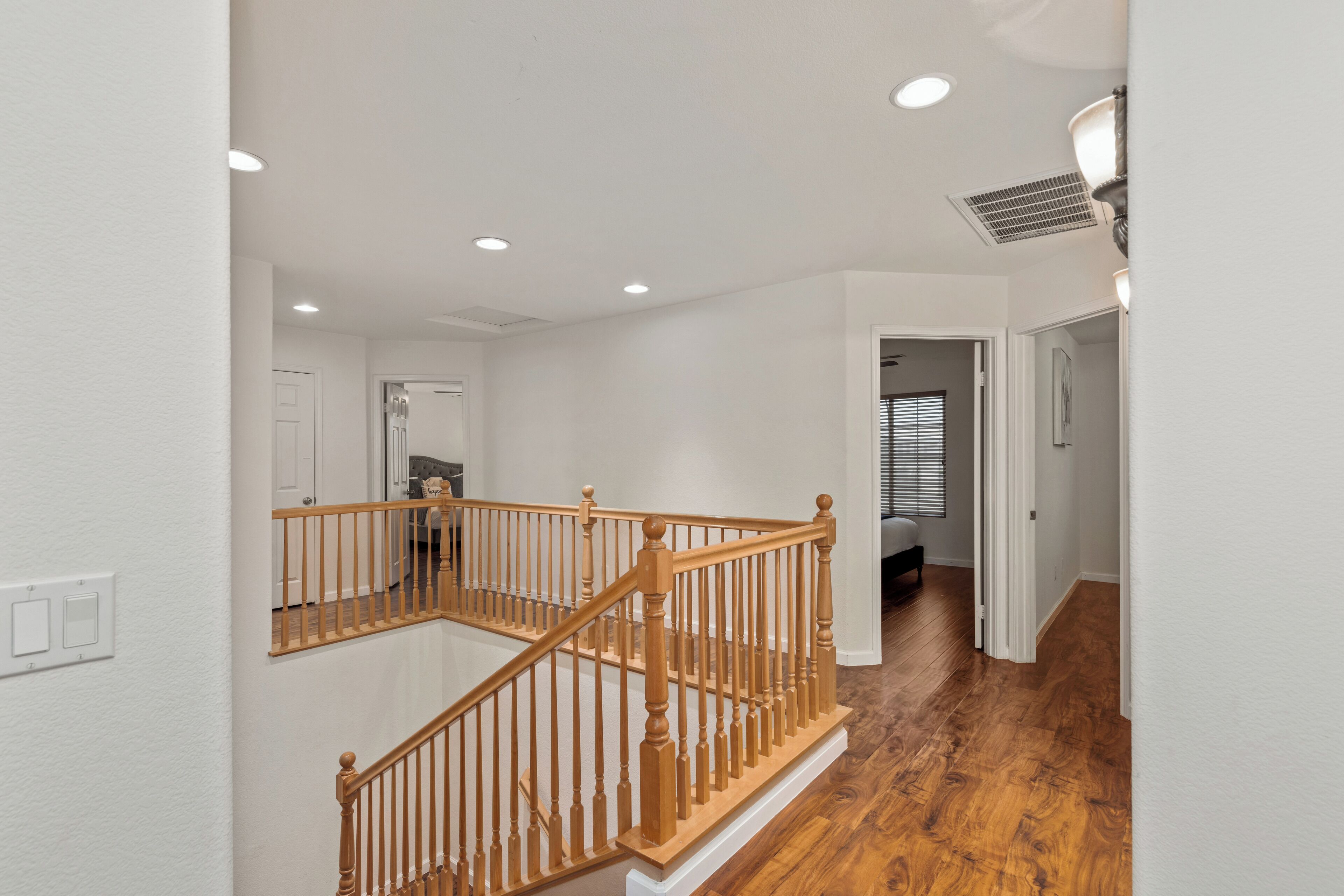 Un intérieur de maison à plusieurs niveaux, avec un escalier en bois, des murs blancs et un couloir menant à une chambre.