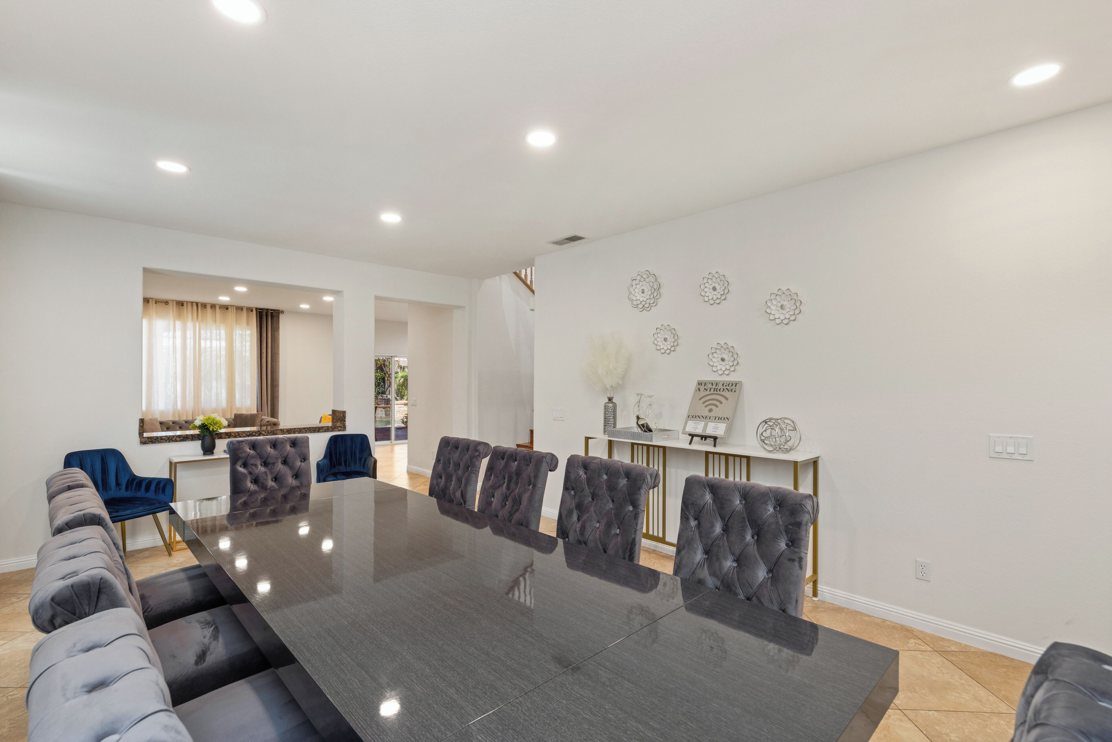 A modern dining area with a long table and upholstered chairs, a kitchen area with a counter, and decorative wall art.